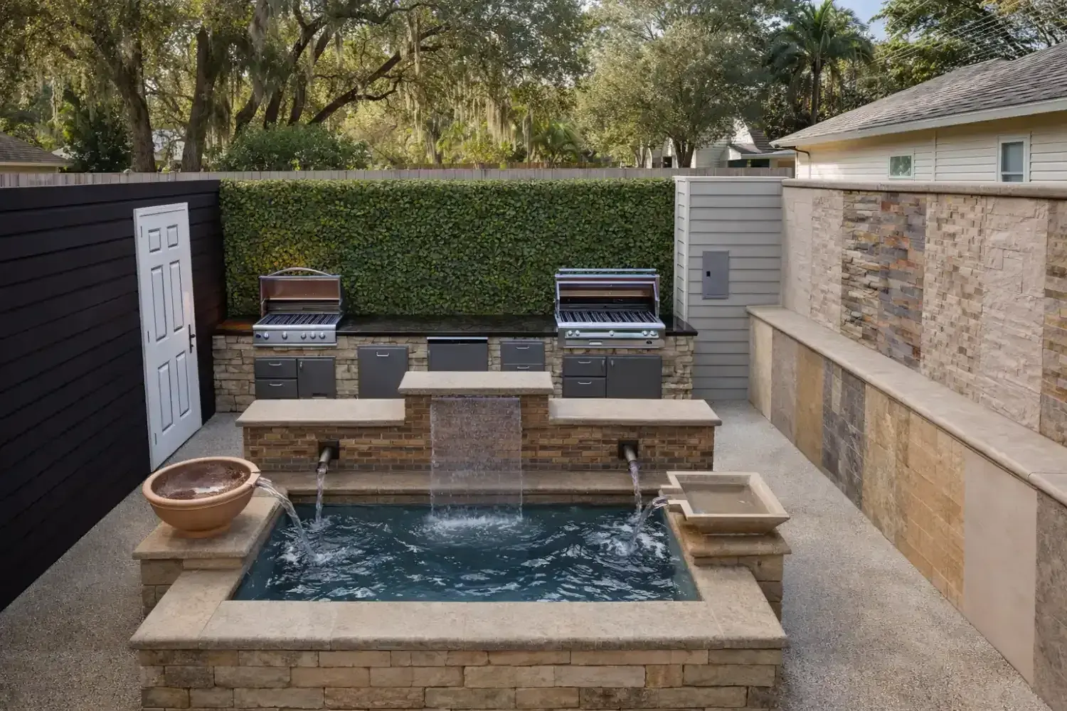 3D rendering: courtyard with a raised spa, water spillways and a grill station against stacked stone